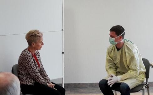 Das Bild zeigt Christine Neu vom Theaterverein Pralka in ihrer Rolle einer "unzufriedenen Patientin" mit einer Besiedlung mit einem multiresistenten Erreger (MRSA). Der Arzt in Schutzausrüstung hatte die Aufgabe trotz der Barrieren von Kittel, Handschuhen und Mundschutz, auf die Emotionen der anspruchsvollen Patientin angemessen zu reagieren. Bild: IKIP