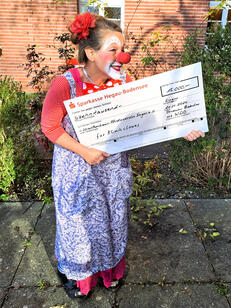 Klinikclownin „Tillie“ mit dem Spendenscheck (Bild: GLKN)